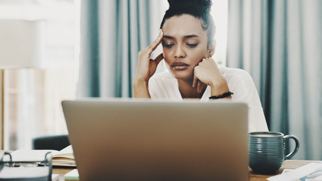 Woman looking at laptop with hand on her forehead in a stressed fashion.